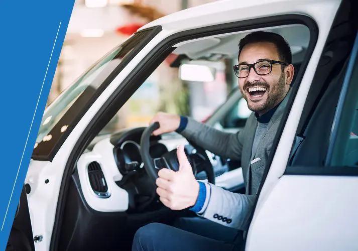 Group 1 A man in a suit sits in a car with the door open, smiling and giving a thumbs-up.